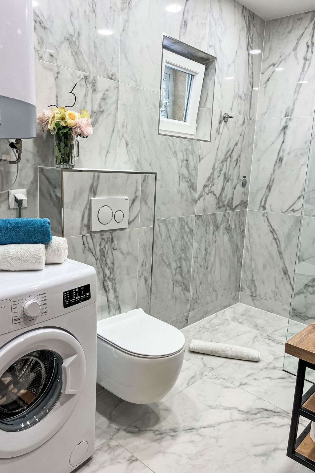 Un baño moderno con suelo de mármol, lavadora, inodoro y zona de ducha.