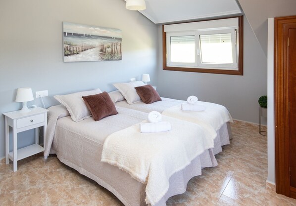 Un dormitorio con dos camas, una mesita de noche, una lámpara, un cuadro y una ventana.