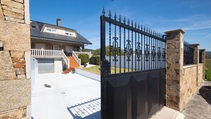 Une allée fermée par un portail mène à une maison dotée d’un mur en pierre et d’un escalier.