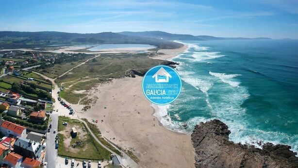 Vue aérienne d’une zone côtière avec une plage, des maisons et un promontoire rocheux.
