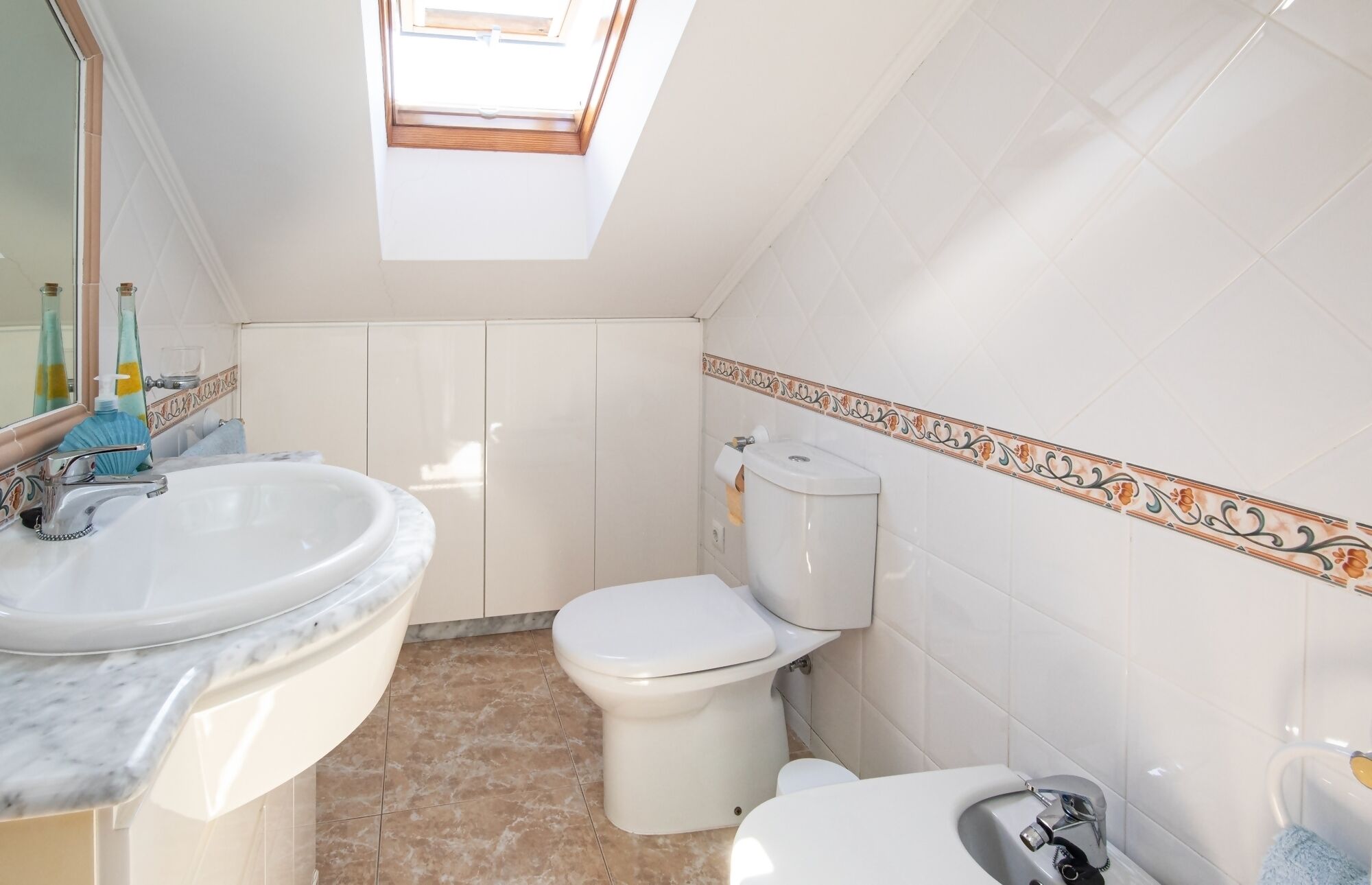 A bathroom with a skylight, a sink, a toilet, and a bidet.
