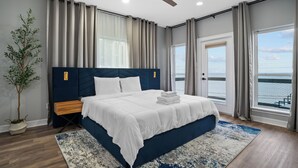 A modern bedroom with a large bed, a ceiling fan, and a view of the sea through the windows. - Waterfront Home w/ Views - Hot Tub + Movie Theatre (Bacliff)