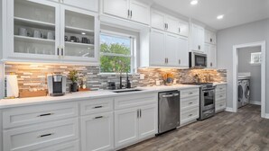 A modern kitchen with white cabinetry, a tiled backsplash, stainless steel appliances, and a view of greenery outside. - Waterfront Home w/ Views - Hot Tub + Movie Theatre (Bacliff)