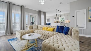 A modern living room with a large sectional sofa, a round coffee table, and a view of the kitchen and dining area in the background. - Waterfront Home w/ Views - Hot Tub + Movie Theatre (Bacliff)