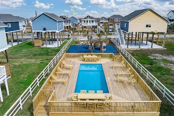 A pool area with wooden deck and lounge chairs, surrounded by beach houses with elevated decks.