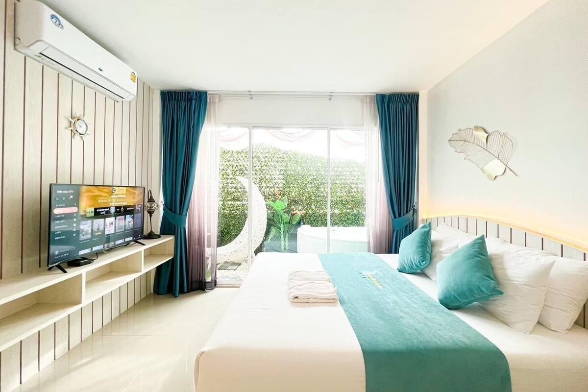 Ein Hotelzimmer mit einem Bett, einem Fernseher auf einem Standfuß, einem Fenster mit Vorhängen und einer Klimaanlage.