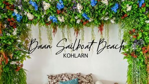 Ein Zimmer mit einer gewebten Bank, gemusterten Kissen und einer Wand mit hängenden Blumenarrangements.