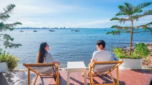 Zwei Personen sitzen an einem kleinen Tisch mit Blick auf das Meer und Boote.