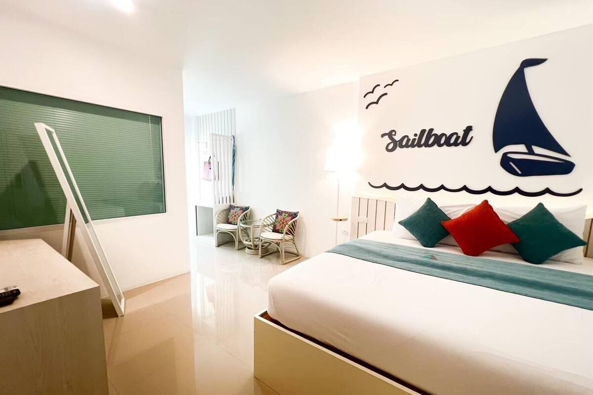 Ein modernes Hotelzimmer mit Bett, Schreibtisch und Stuhl. Eine große Wanddekoration zeigt das Wort "Sailboat" und ein Bild eines Segelbootes.