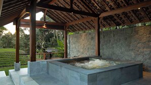 Un área de spa con pared de piedra, una bañera de hidromasaje y una estructura de techo de madera.