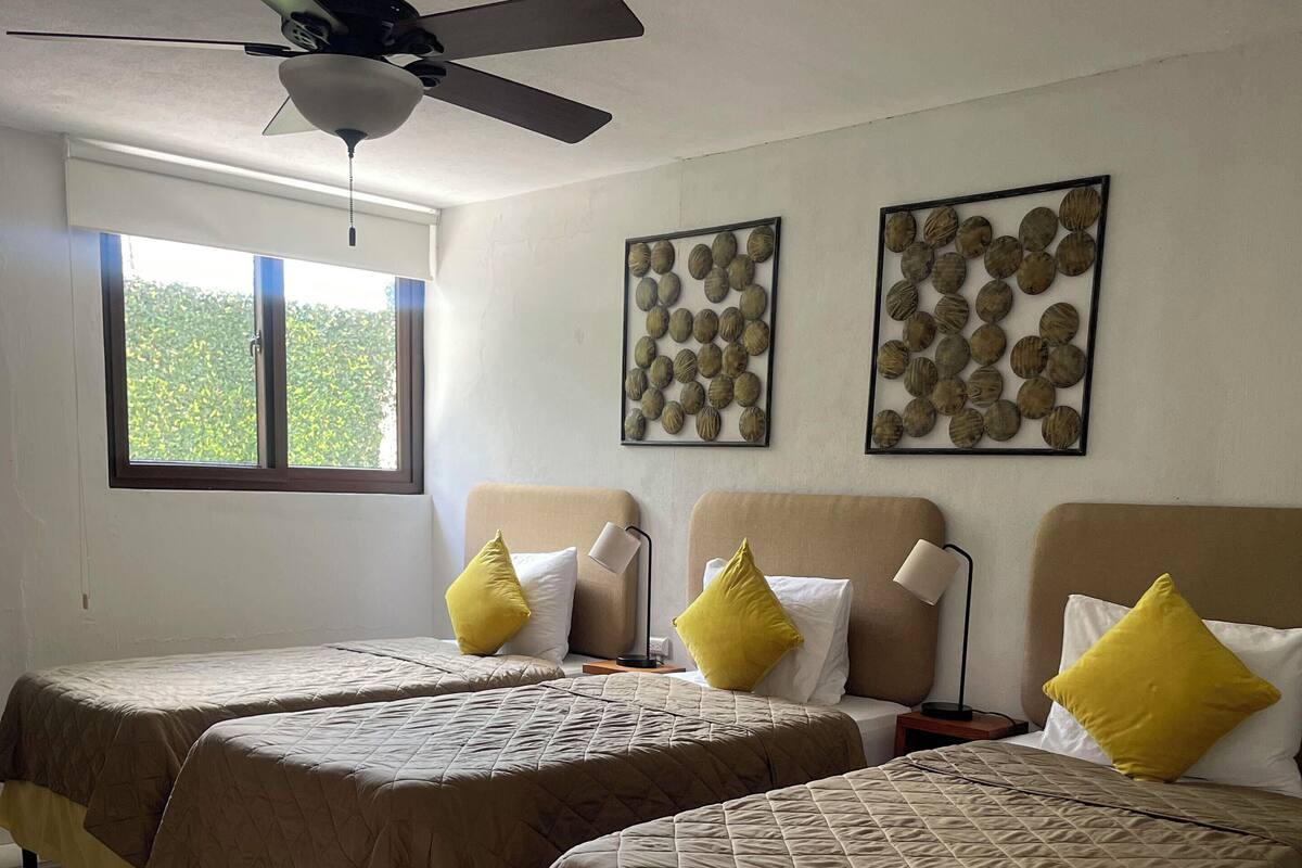 Een hotelkamer met twee bedden, een plafondventilator, een raam met uitzicht op groen en twee decoratieve items aan de muur.
