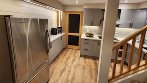 Una cocina moderna con refrigerador de acero inoxidable, piso de madera y gabinetes grises.