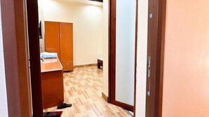 Um corredor com um armário de madeira, uma mesinha com cadeira e uma porta com painel de vidro jateado.