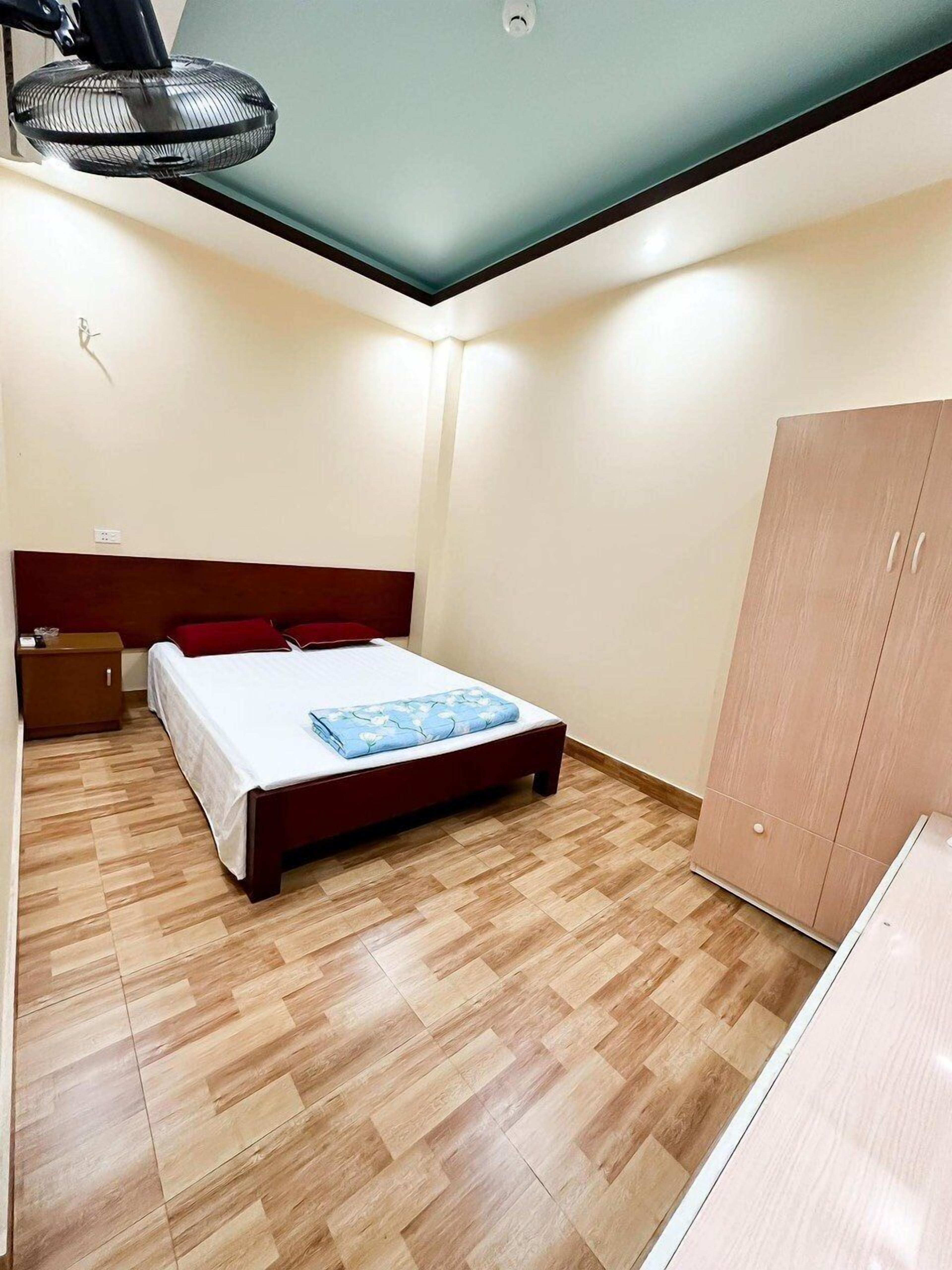 A bedroom with a bed, wooden wardrobe, and a ceiling fan.