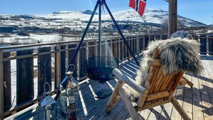 Une terrasse en bois avec une chaise et une lanterne suspendue, un barbecue en métal et un drapeau.