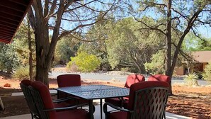 An outdoor patio with a metal table and chairs, surrounded by trees and a clear view of the road. - Luxe Serenity - Remodeled home walking distance from Chapel of the Holy Cross.
 (Sedona)