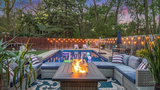 A backyard with a swimming pool, outdoor seating, and string lights. - Paradise Pool House (Omaha)