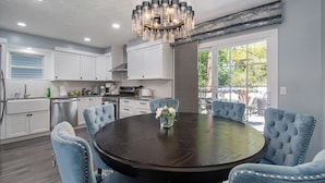 A modern kitchen with white cabinets, a dark wooden dining table, and a chandelier. - Paradise Pool House (Omaha)