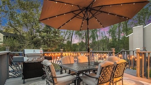 An outdoor patio with a grill, dining table, chairs, and string lights. - Paradise Pool House (Omaha)