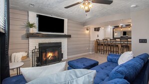 A living room with a fireplace, blue sofa, and a ceiling fan. - Paradise Pool House (Omaha)