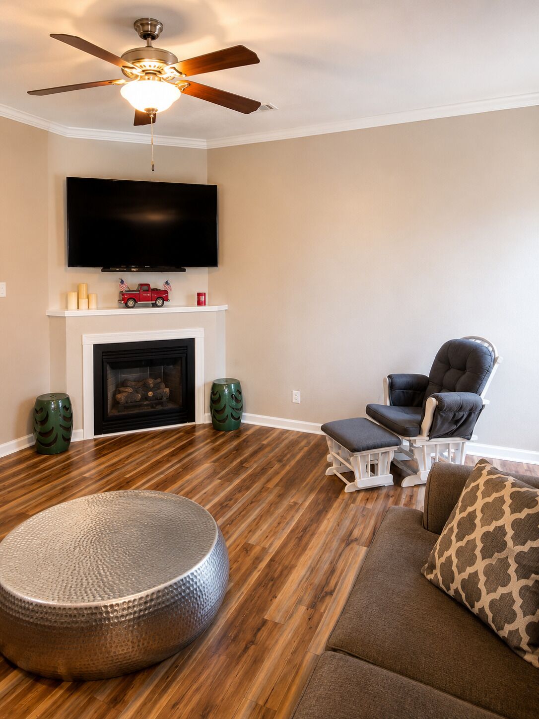 A living room with a fireplace, a ceiling fan, a television, and a seating area.