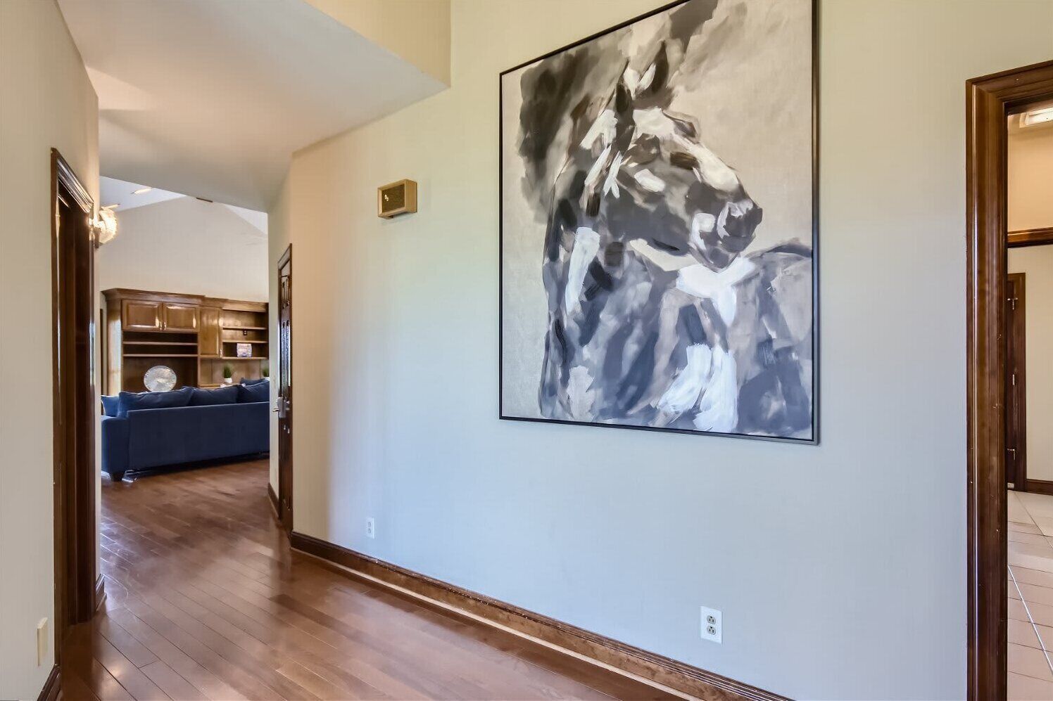 A hallway with a large abstract painting, wooden flooring, and a blue sofa in the background.
