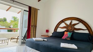 A bedroom with a large bed, a wooden headboard, a sliding glass door to a balcony, and a view of greenery outside. - Basic 3 bedroom villa (Playa del Carmen)