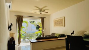 A room with a ceiling fan, a bed with pillows, a desk with a chair, a window with curtains, and a wall-mounted artwork. - Basic 3 bedroom villa (Playa del Carmen)