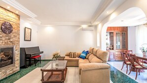 Un salón espacioso con un sofá seccional, una mesa de centro de vidrio, una chimenea, un piano y una zona de comedor con muebles de madera.