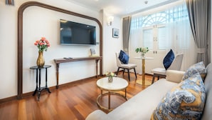 A modern living room with a flat-screen TV, a sofa, a coffee table, and a small round table with flowers. - Cherie Bangkok Boutique Hotel (Bangkok)
