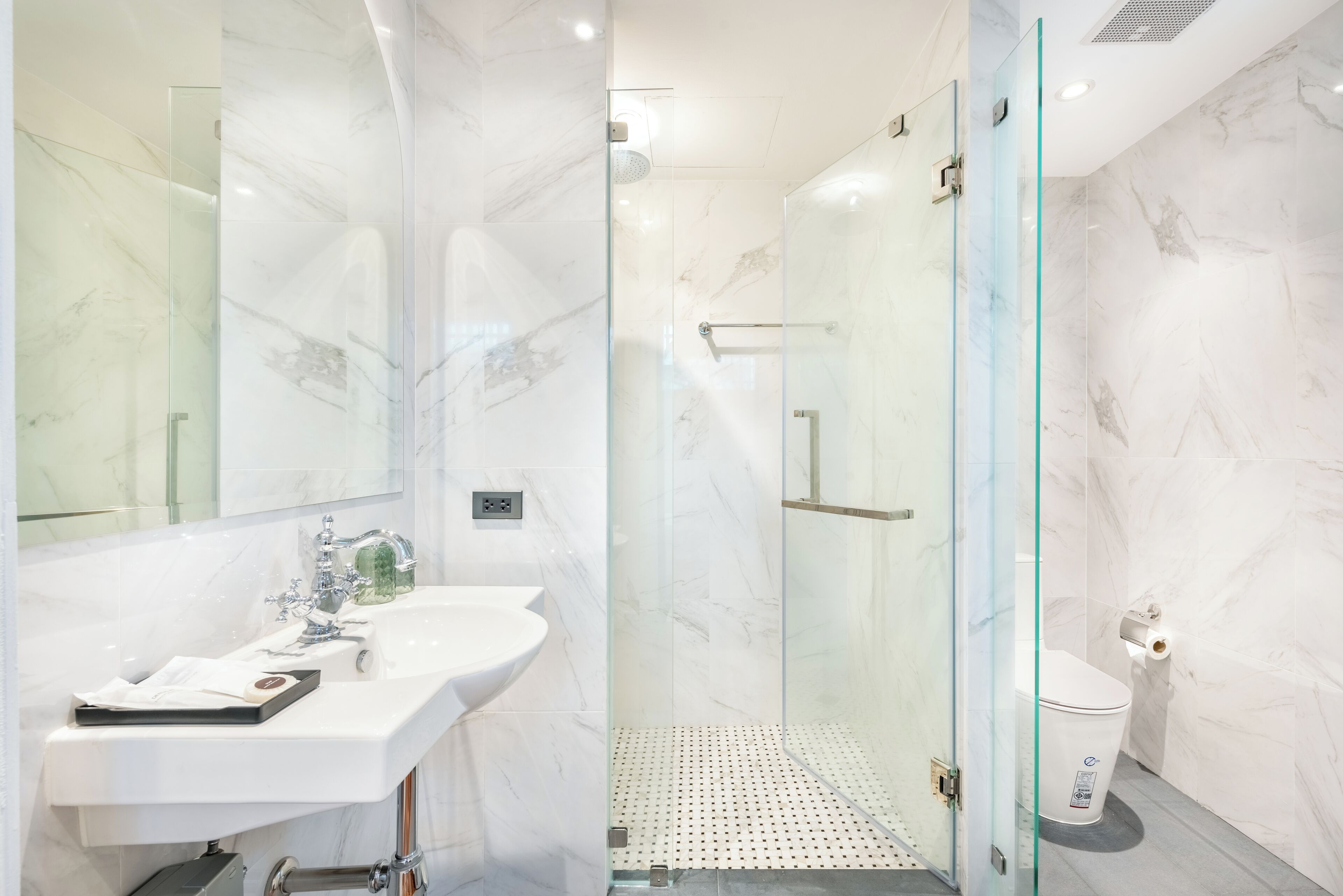 A modern bathroom with a glass-enclosed shower, a white sink, and a toilet.