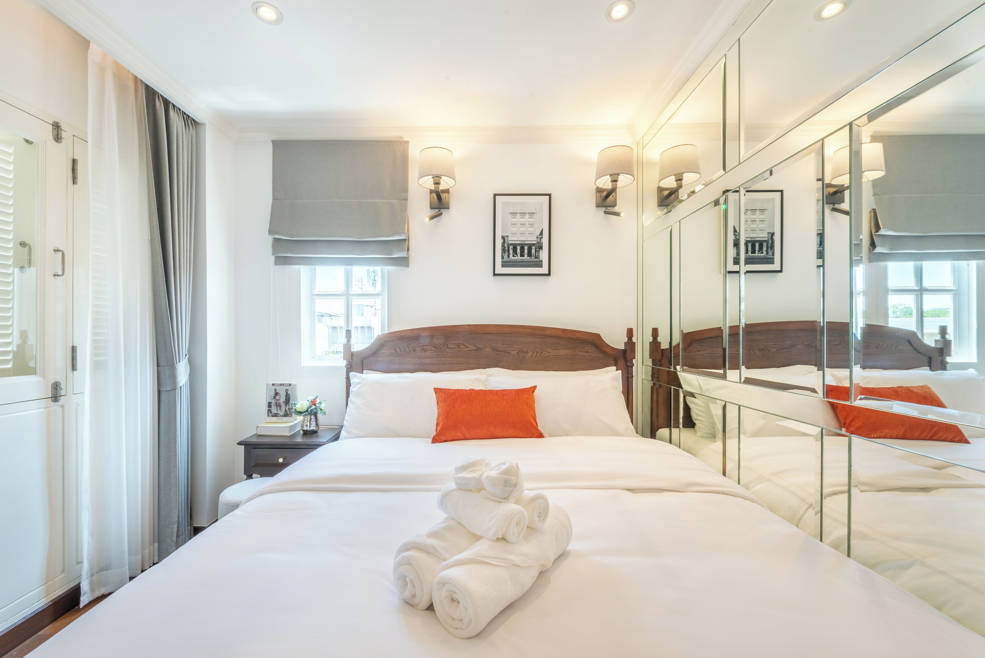 A hotel room with a large bed, a nightstand, a mirror, and a window with curtains.