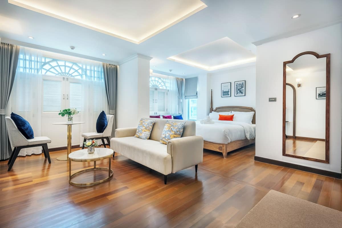 Une chambre d’hôtel moderne avec un canapé, une table basse ronde, un lit et un grand miroir.