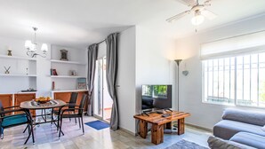 A modern living room with a sofa, a TV, a wooden coffee table, and a dining area with chairs and a table. - Los almendros by Interhome (Rincón de la Victoria)