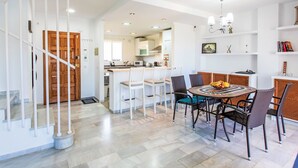 A modern kitchen with white cabinets, a dining area with a round table, and a staircase with white railings. - Los almendros by Interhome (Rincón de la Victoria)