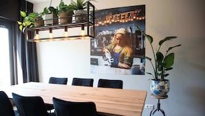 A dining area with a wooden table, black chairs, potted plants, and a wall-mounted light fixture. - House 'n Cheese - Alkmaar (Alkmaar)