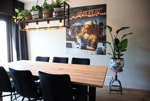 A dining area with a wooden table, black chairs, potted plants, and a wall-mounted light fixture.