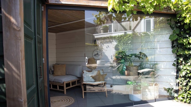 A glass door entrance to a room with a wicker chair, a cushion, and a small table. - House 'n Cheese - Alkmaar (Alkmaar)