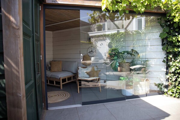 A glass door entrance to a room with a wicker chair, a cushion, and a small table.