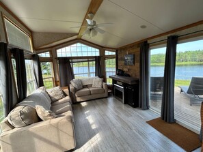 A spacious living room with a large window, a ceiling fan, and a view of a lake. - Private Waterfront Getaway (Richibouctou)
