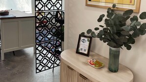 A modern kitchen with a white cabinet, a decorative black metal partition, a framed black panther artwork, and a vase with green leaves on a wooden console table.