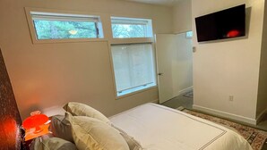 A bedroom with a bed, a ceiling fan, a TV mounted on the wall, and two windows.