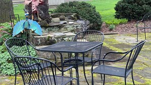A patio with a table and four chairs, surrounded by a stone pathway and greenery.
