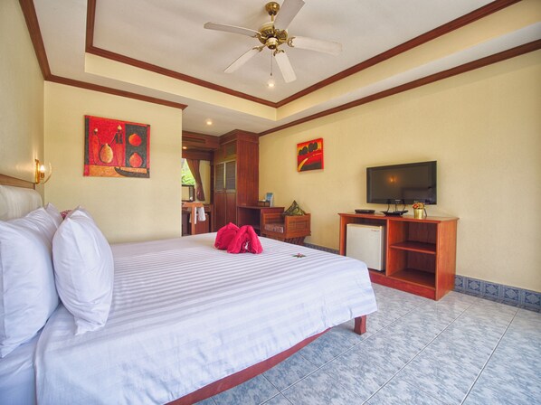 Habitación de hotel con una cama grande, ventilador de techo, televisor y obras de arte en las paredes.