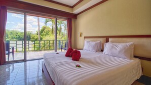 A hotel room with a large bed, a view of a balcony with a pool, and a tropical landscape.