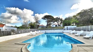 A rectangular swimming pool with a tiled deck, surrounded by white lounge chairs and a wooden fence. - Les Cariatides by Interhome (Ile d'Oléron)