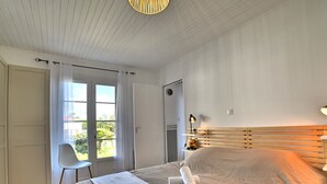 A bedroom with a large bed, a chair, a desk, and a window with curtains. - Les Cariatides by Interhome (Ile d'Oléron)