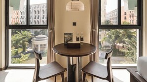 Un comedor con una mesa redonda, dos sillas, una lámpara colgante y ventanas grandes con cortinas.