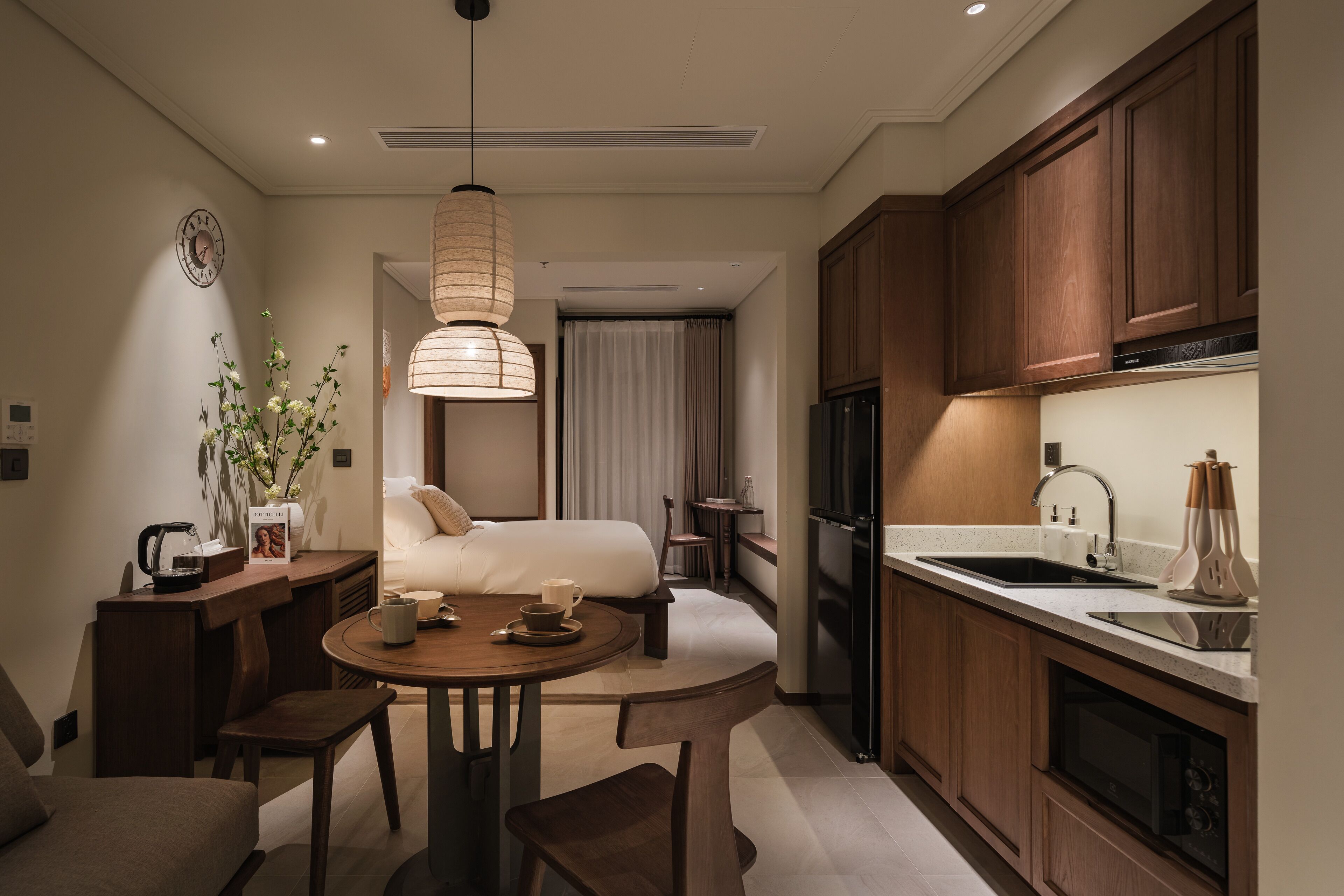 A modern hotel room with a kitchenette, a dining area, and a bed.