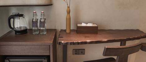 Una kitchenette con cafetera, dos botellas de agua, un florero con flores, una caja de pañuelos y una silla de madera.
